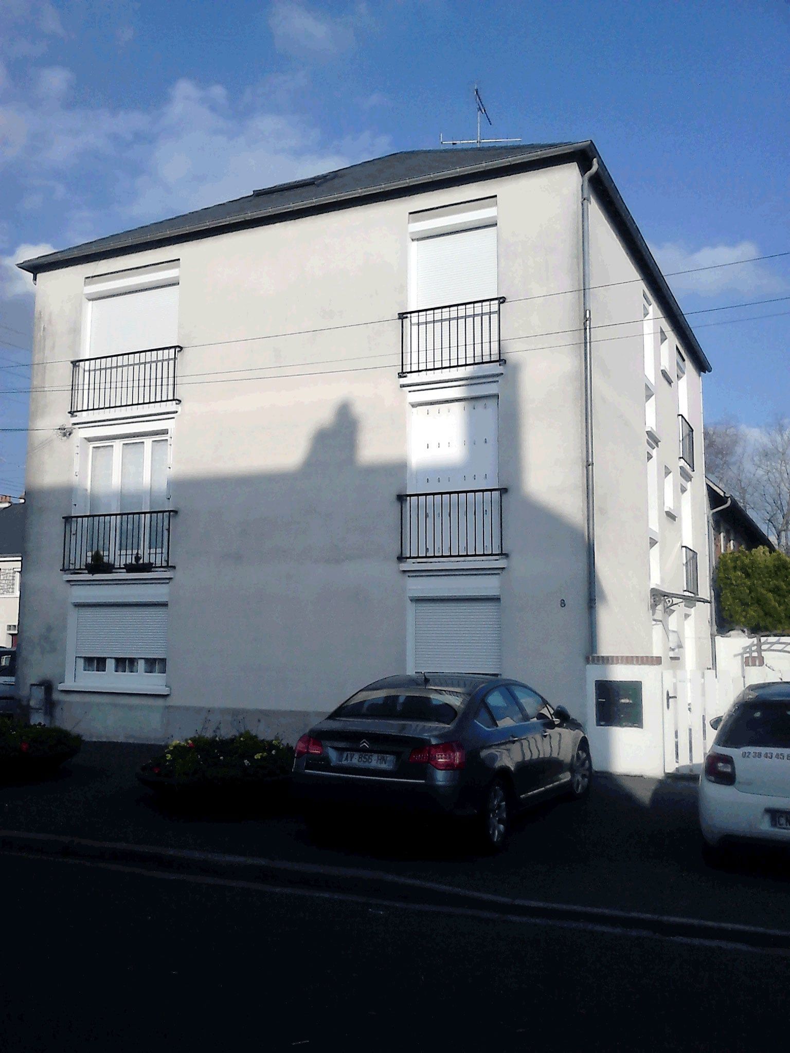 Immeuble d'appartements blanc avec des voitures garées à un coin de rue ensoleillé