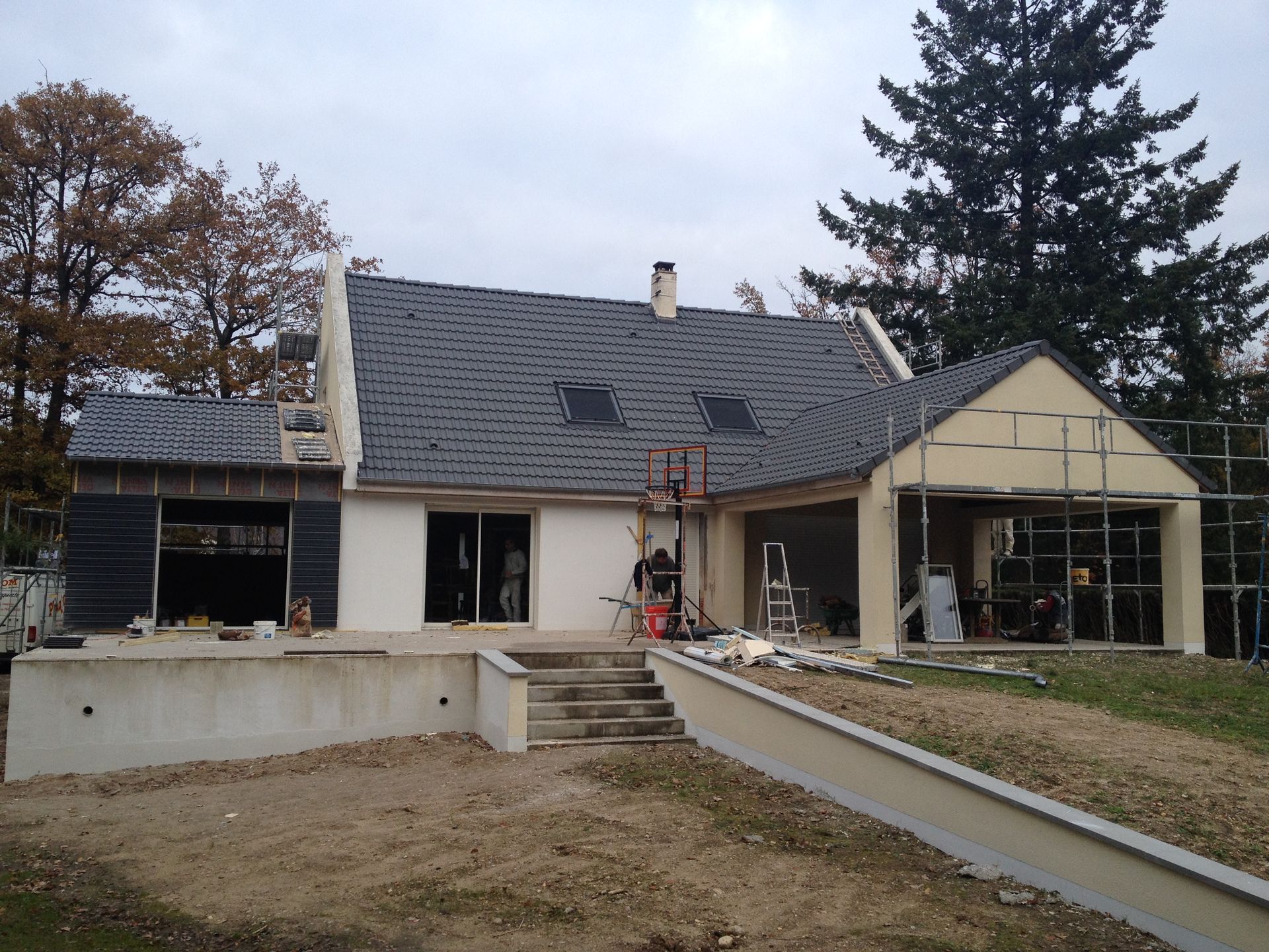 Extérieur de la maison avec un toit sombre, des murs blancs et une allée en pente devant.