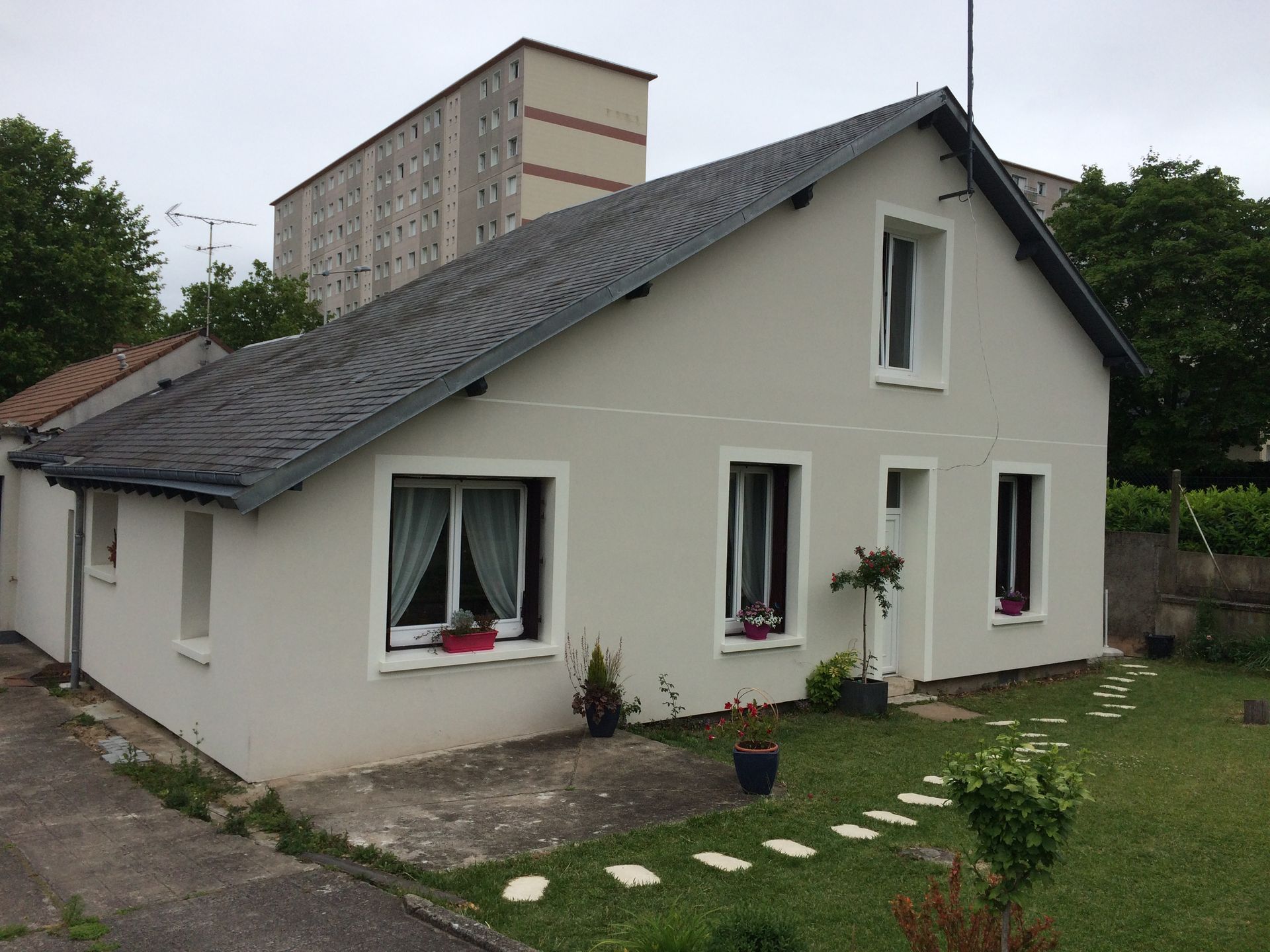 Maison blanche au toit sombre et au petit jardin, vue depuis la cour avant