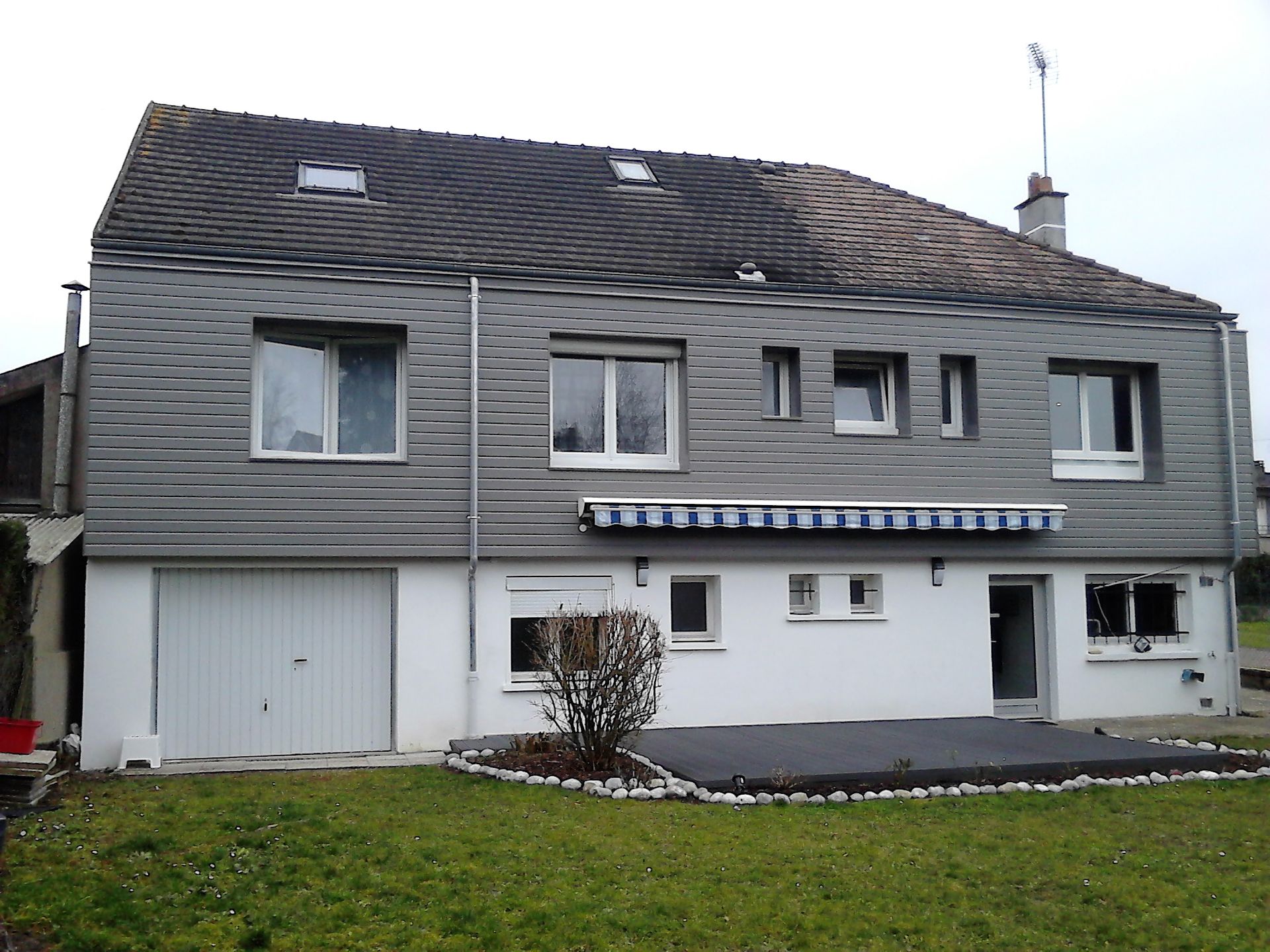 Maison grise à deux étages avec garage, lucarnes et petite pelouse à l'avant.