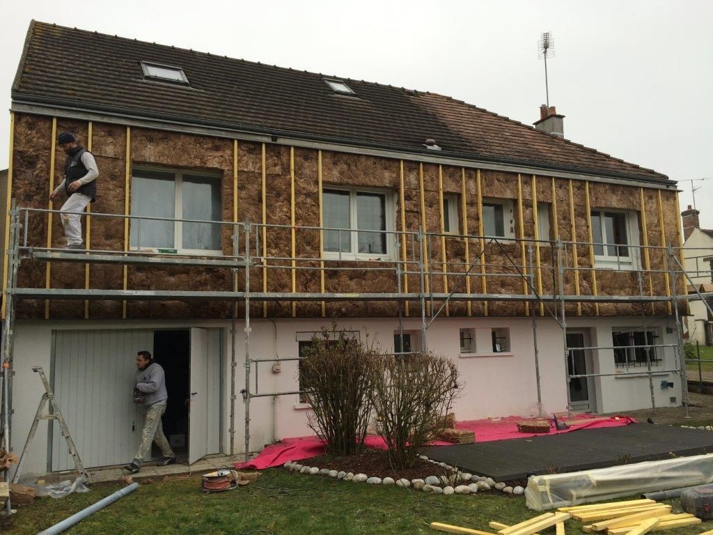 Extérieur de la maison avec des échafaudages et des ouvriers effectuant des réparations sur le toit et la façade.
