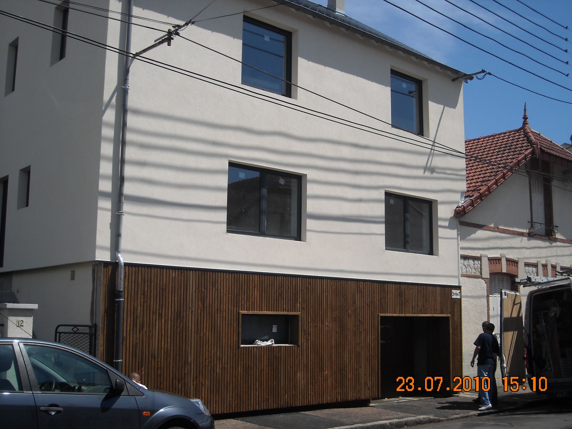 Maison blanche moderne avec bardage en bois foncé et vue sur la rue sous un ciel bleu clair