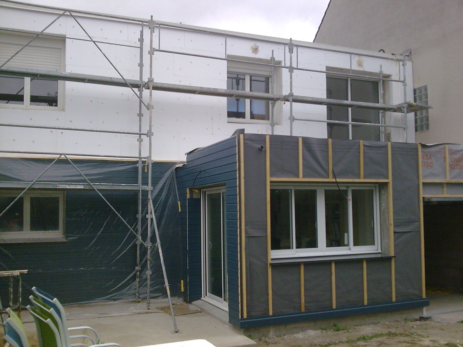 Façade du bâtiment en rénovation, avec des échafaudages et une structure fermée bleue et grise en façade.