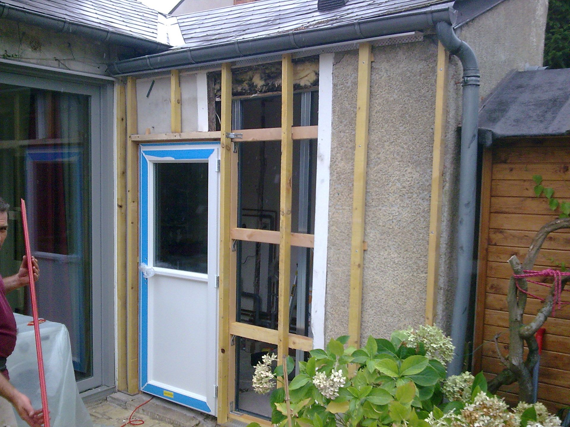 Porte partiellement construite avec des encadrements bleus à côté d'un jardin et d'une clôture en bois
