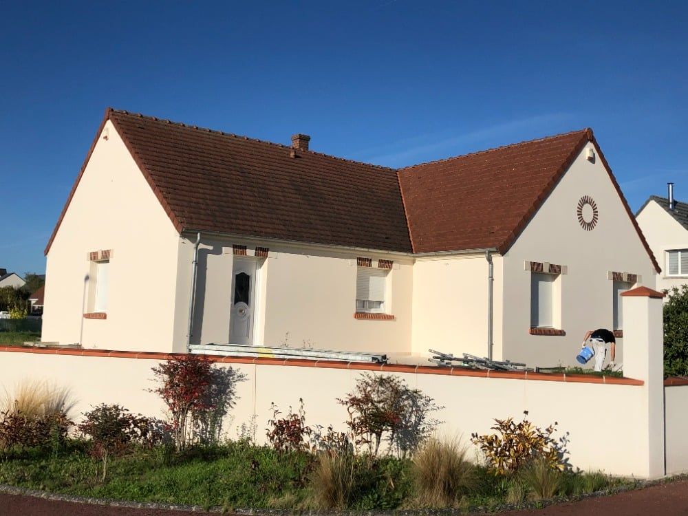 Maison blanche au toit rouge et aux murs couleur crème, jardin de devant, sous un ciel bleu limpide