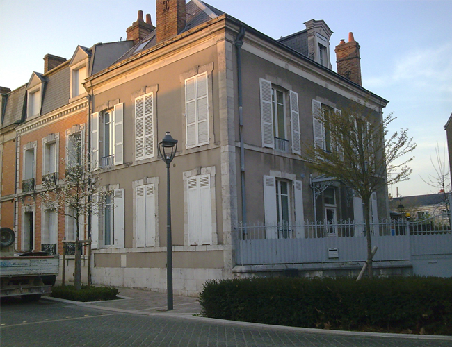 Manoir historique beige avec volets blancs et porche au coucher du soleil