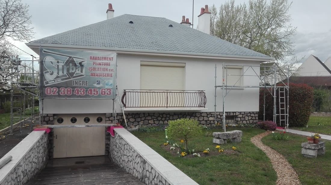 Petite maison blanche avec rampe d'accès et cour, recouverte d'une bâche grise par un jour de pluie