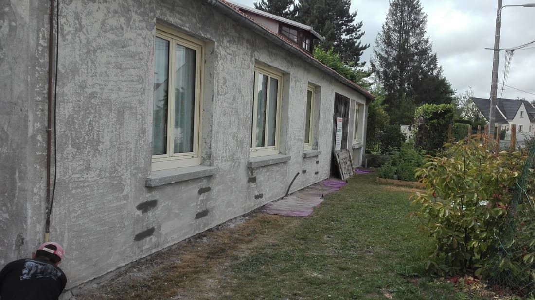 Façade de maison grise patinée par le temps, fenêtres à cadre blanc, allée de jardin étroite et ciel couvert