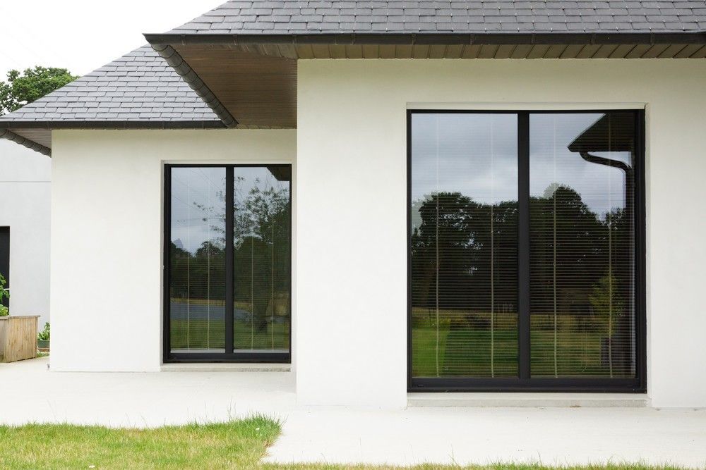 Extérieur de maison moderne avec murs blancs, toit foncé et grandes fenêtres allant du sol au plafond
