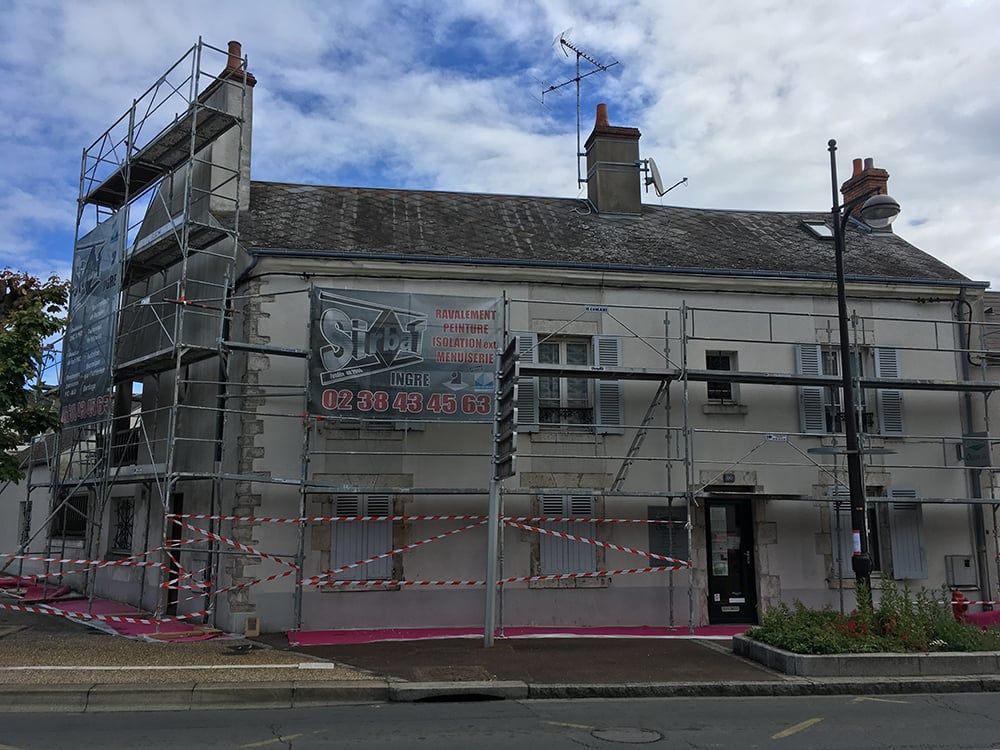 Échafaudages autour d'un bâtiment blanc en rénovation, avec une barrière rouge et blanche au niveau de la rue.