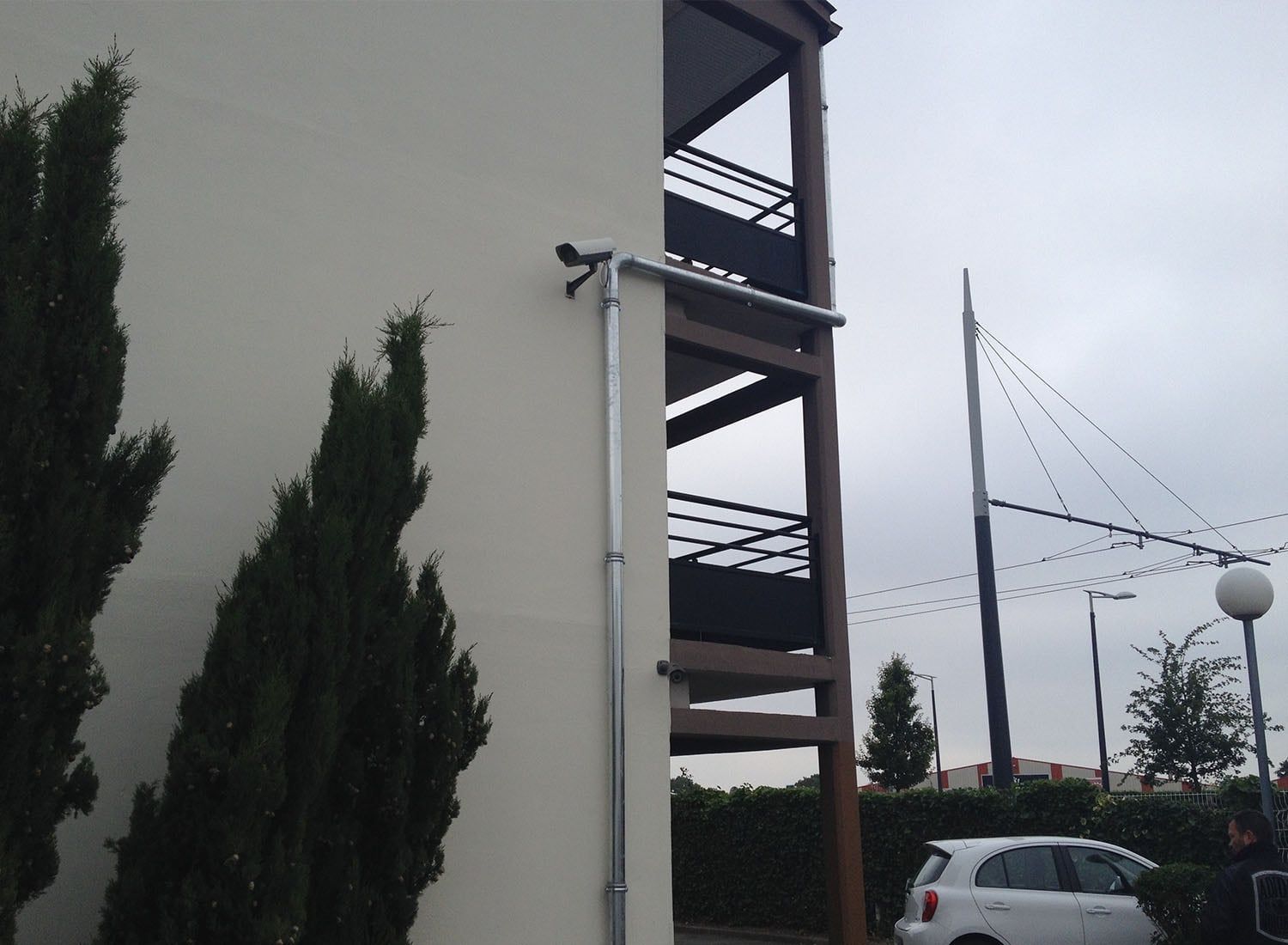 Extérieur d'un appartement avec balcons, arbres, voiture garée et ciel couvert