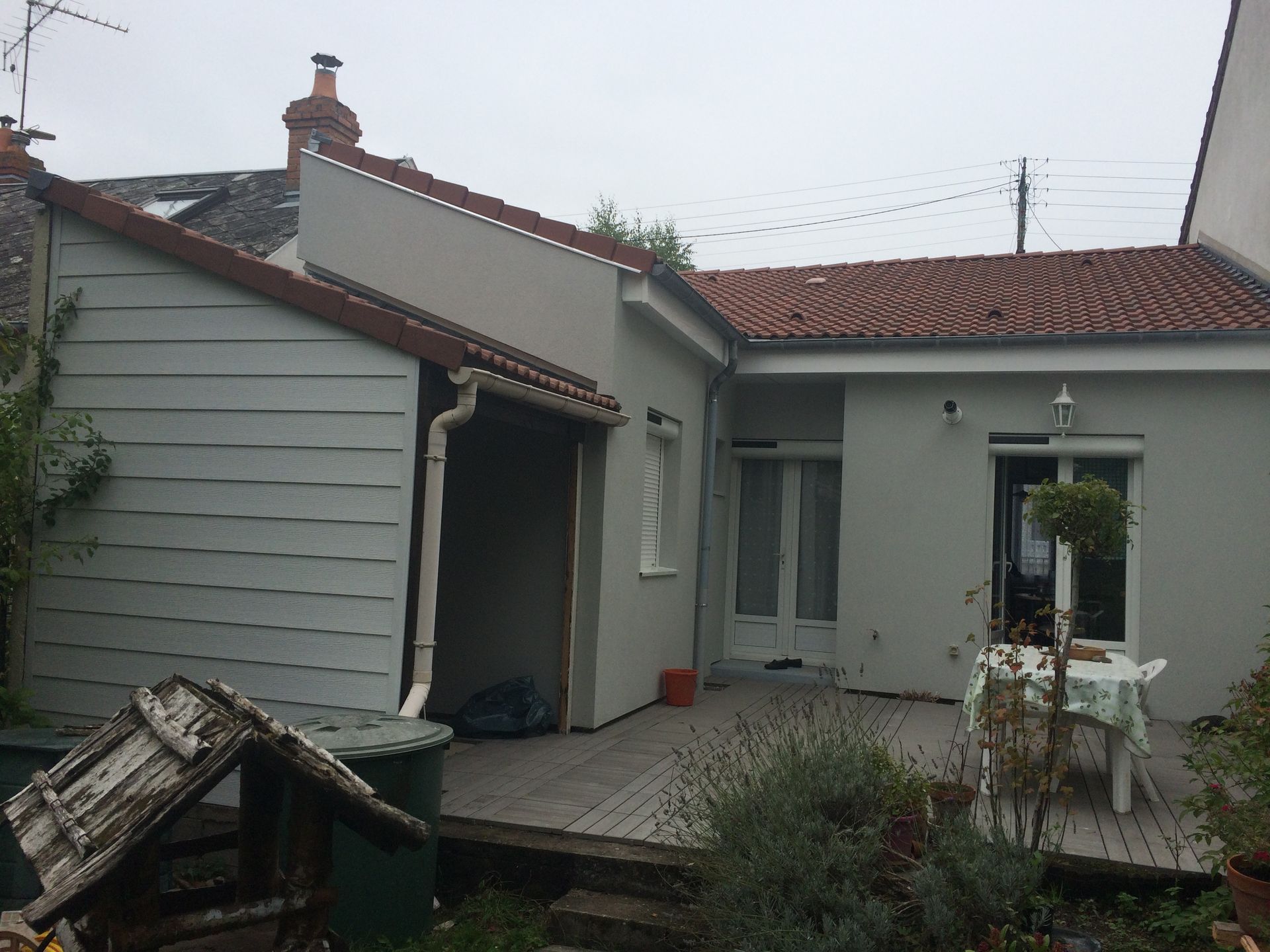 Cour intérieure d'une petite maison grise avec toit rouge, terrasse et plantes en pot