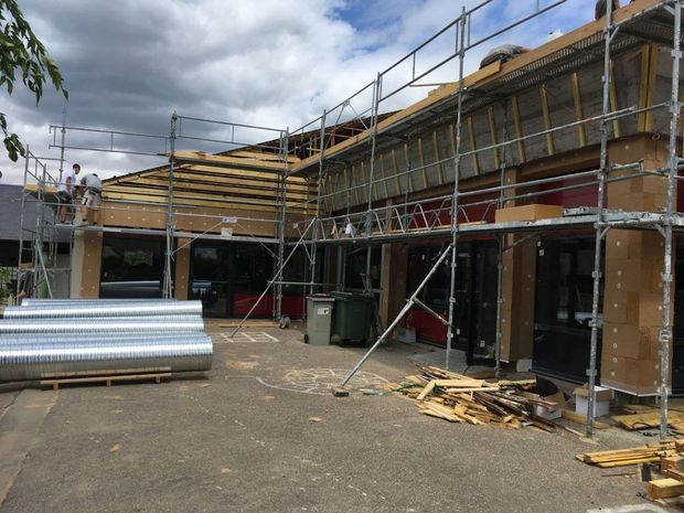 Bâtiment en construction avec échafaudages, charpente et matériaux de toiture apparents au premier plan.