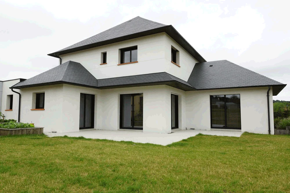 Maison moderne blanche de deux étages avec un toit foncé et de grandes fenêtres donnant sur une pelouse verte