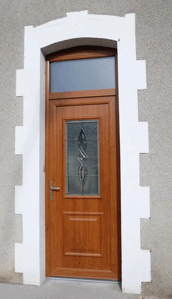 Porte d'entrée en bois avec panneau en verre dépoli dans un encadrement de porte en pierre blanche et grise