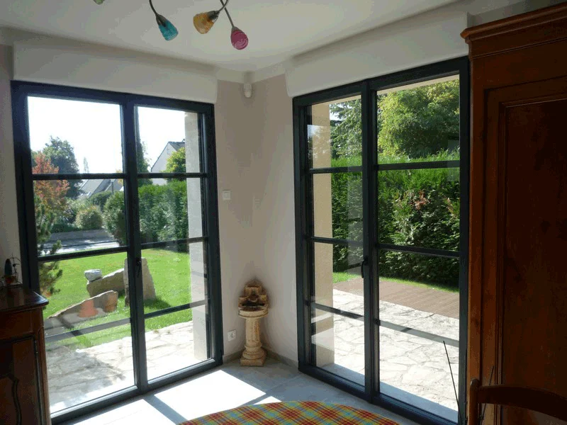 Pièce baignée de soleil avec portes vitrées à cadre noir donnant sur un patio-jardin verdoyant.
