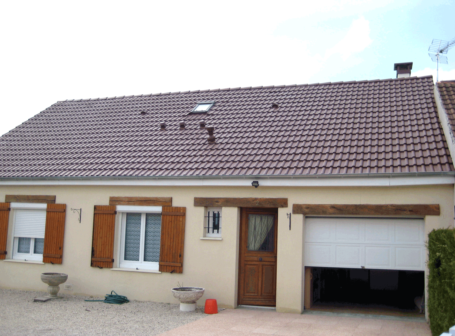 Maison beige de plain-pied avec toit marron, fenêtres à volets, porte d'entrée et garage ouvert.
