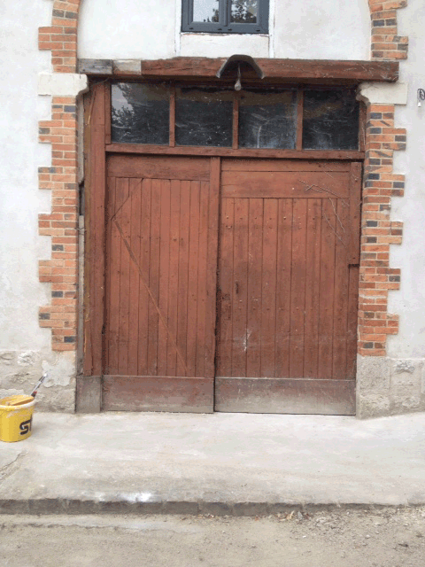 Double porte en bois sur une façade en pierre, avec un petit seau jaune sur le côté gauche.