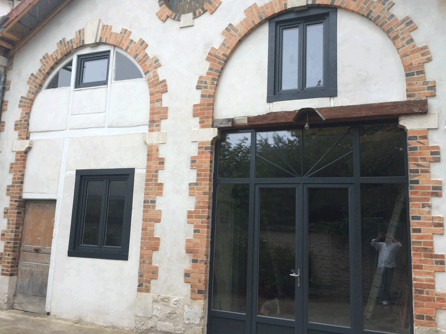 Façade en pierre avec fenêtres cintrées et porte de magasin noire sous un encadrement en briques