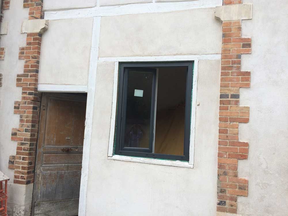 Mur partiellement fini avec une fenêtre et une porte, laissant apparaître la brique et le stuc.