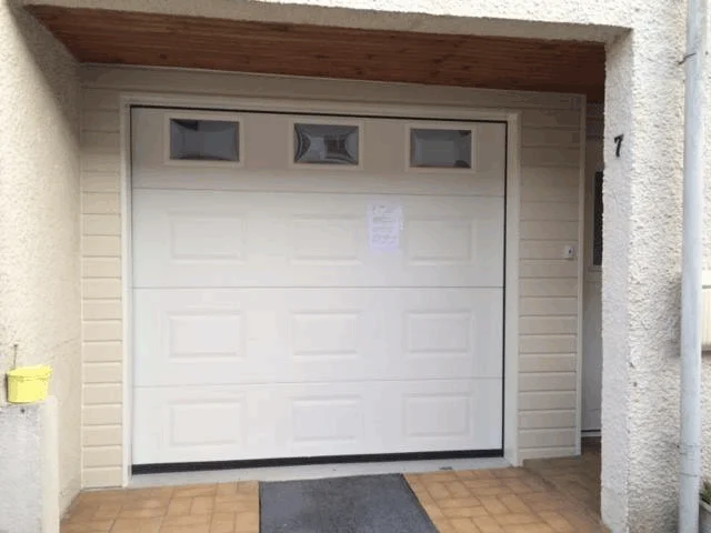 Porte de garage blanche avec petites fenêtres sur un bâtiment extérieur en stuc beige.