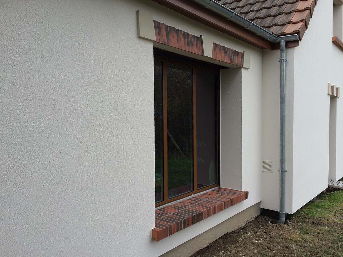Fenêtre extérieure avec encadrement marron et appui en brique sur une maison en stuc blanc