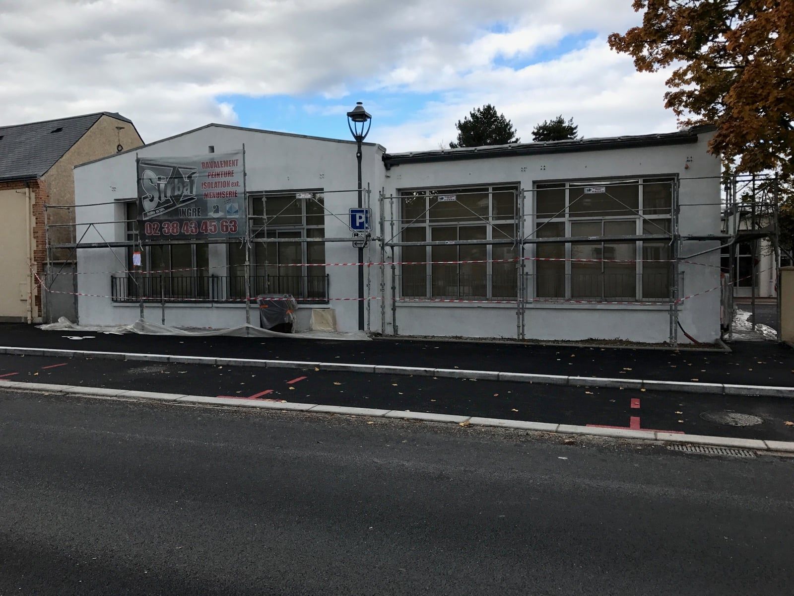 Petite boutique blanche avec de grandes vitrines, un parking devant et un lampadaire sur le trottoir.
