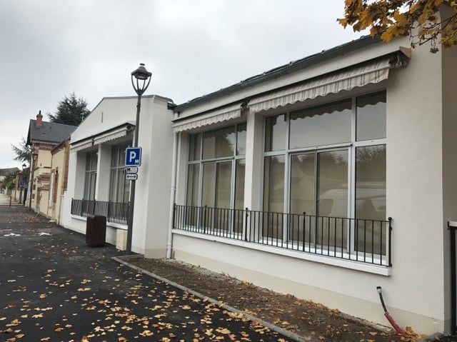 Façade blanche avec de grandes fenêtres et un trottoir donnant sur une rue pluvieuse et jonchée de feuilles.