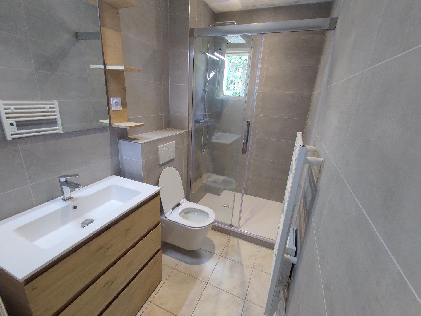 Salle de bains moderne avec meuble lavabo en bois, toilettes, douche en verre et murs carrelés gris