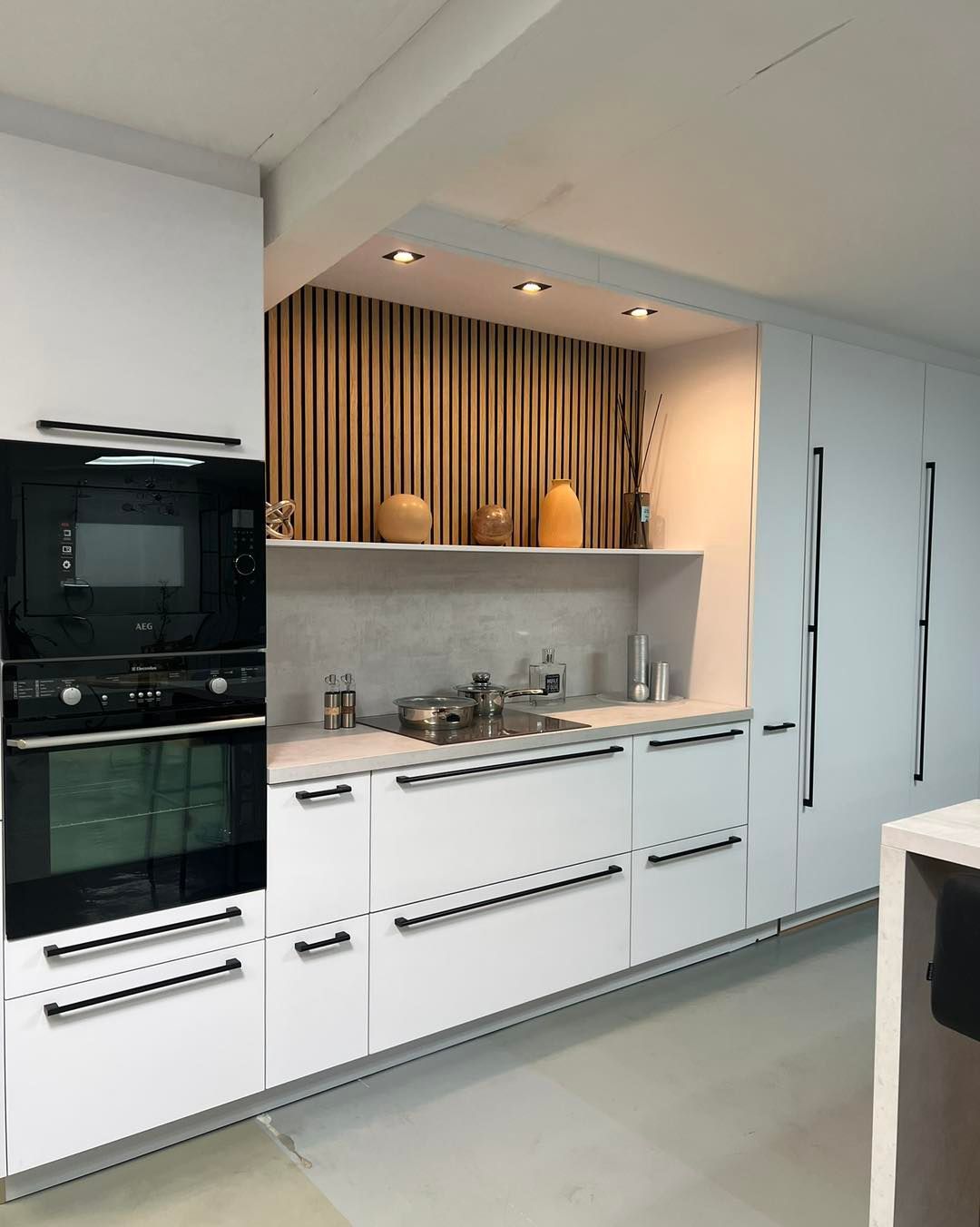 Cuisine blanche moderne avec des parties en bois, fours encastrés, évier en inox et éclairage indirect