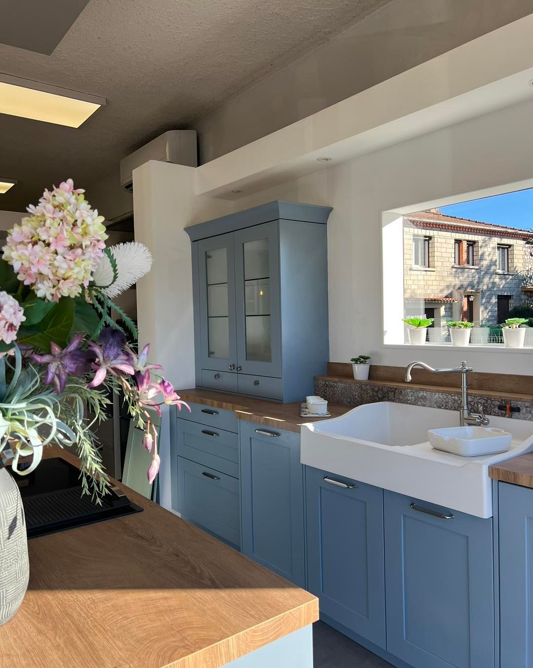 Cuisine moderne avec placards bleus, évier de style ferme blanc et vase de fleurs sur un comptoir en bois