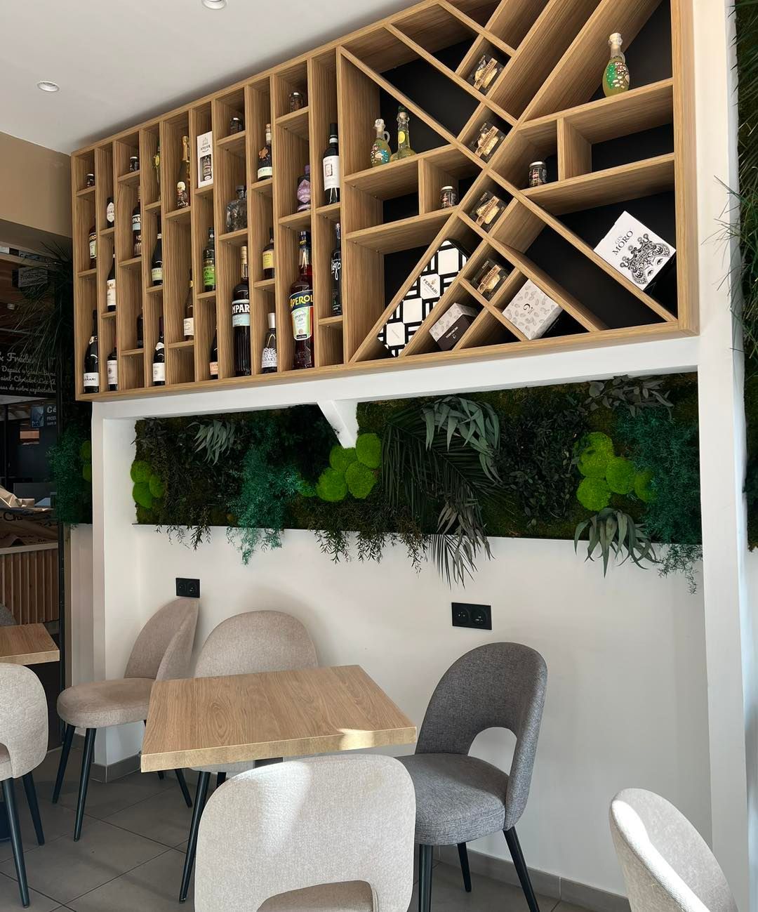 Intérieur d'un café avec étagères penchées en bois, plantes suspendues et petites tables avec chaises blanches et grises