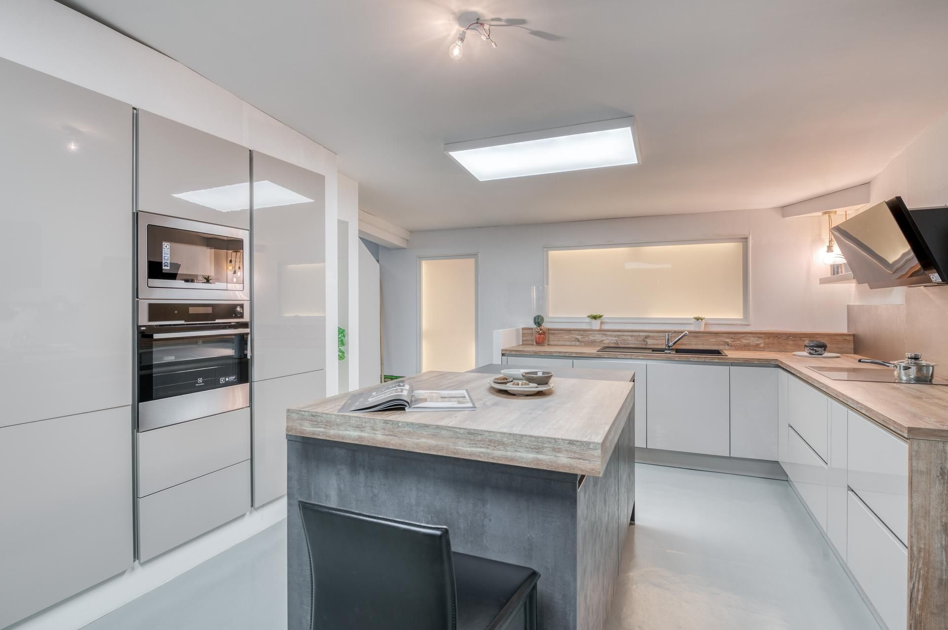 Cuisine blanche moderne avec îlot central, four encastré et éclairage zénithal lumineux