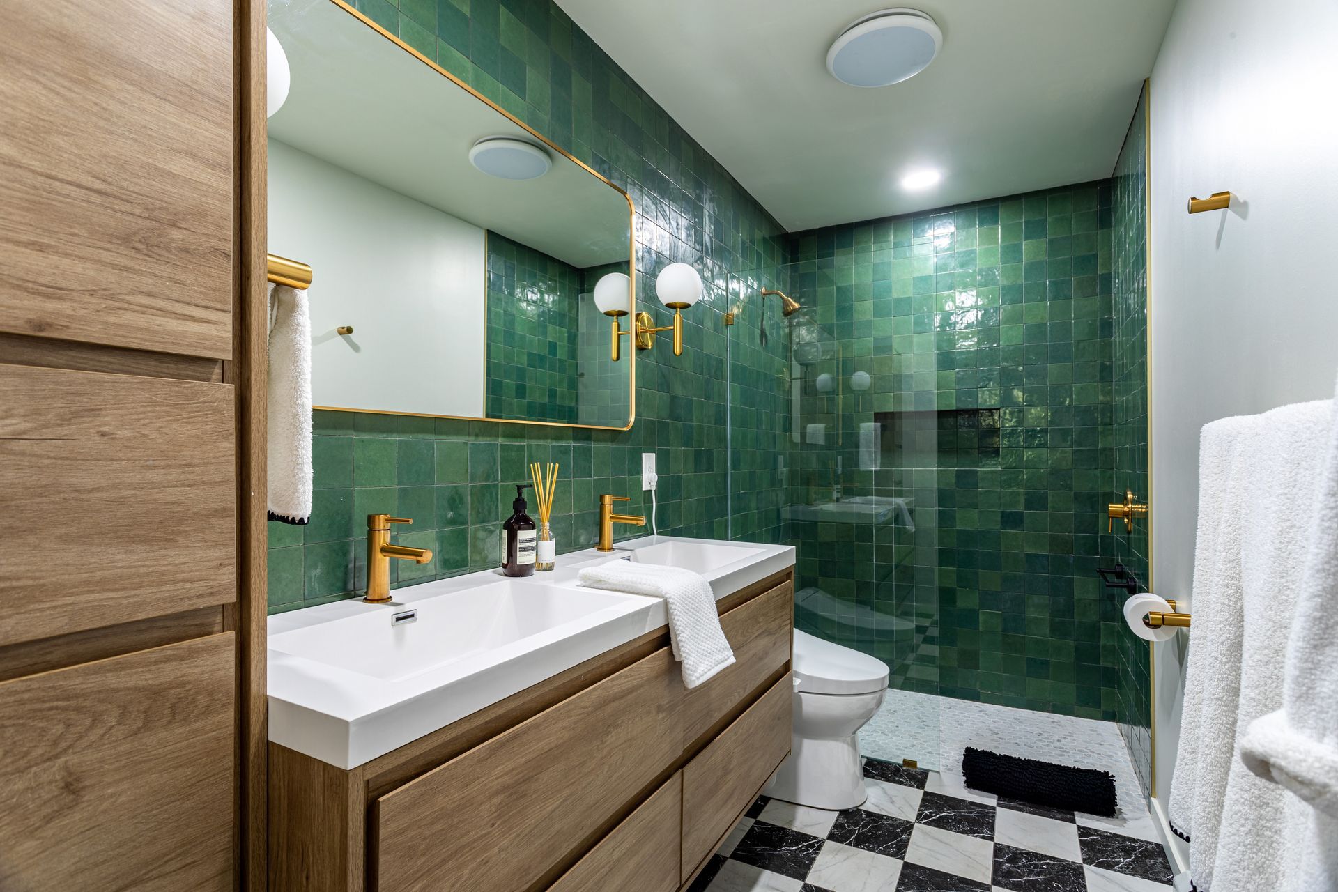 Salle de bains moderne avec douche carrelée de vert, meuble lavabo double vasque et carrelage au sol noir et blanc