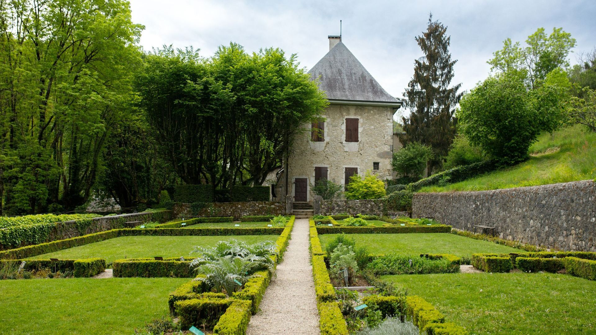 Façade d'une petite maison en pierre avec beaucoup de verdure autour
