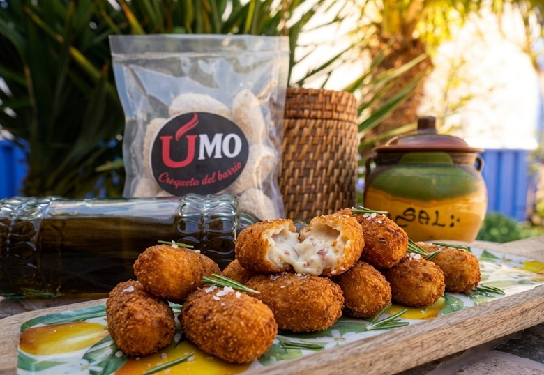 Un plato de croquetas fritas doradas, servidas con un pequeño cuenco de salsa para mojar, rodajas de limón y perejil fresco.