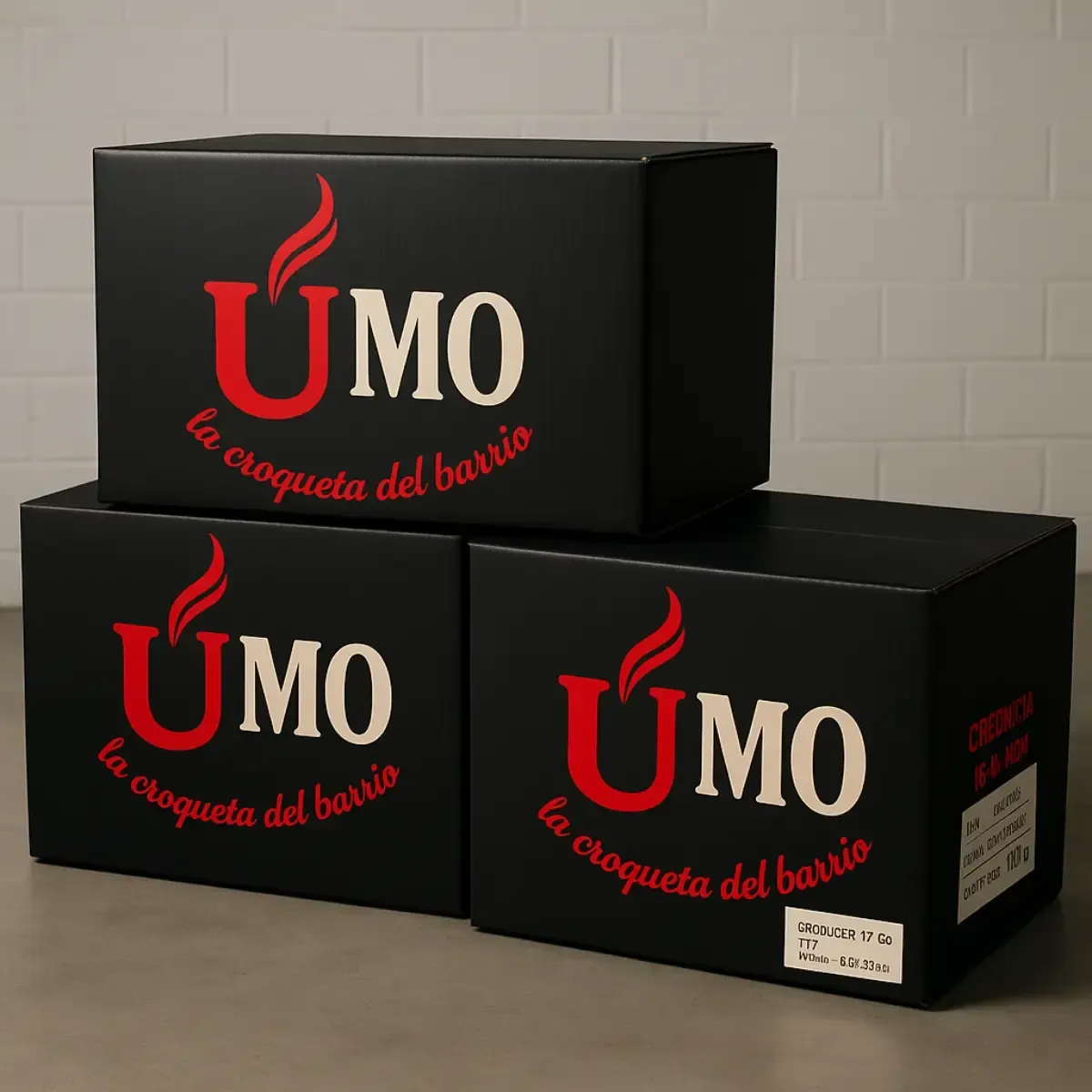 Tres cajas de cartón negras apiladas en el suelo, cada una impresa con el logotipo rojo y crema