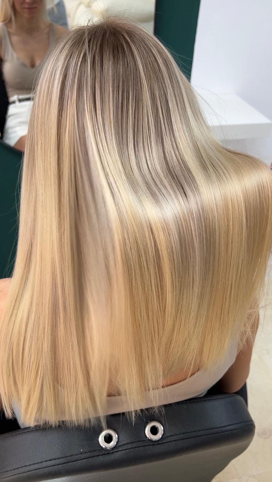 Una mujer con cabello largo y rubio está parada frente a una pared verde.