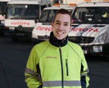 Un hombre con una chaqueta amarilla está parado frente a una fila de furgonetas blancas.