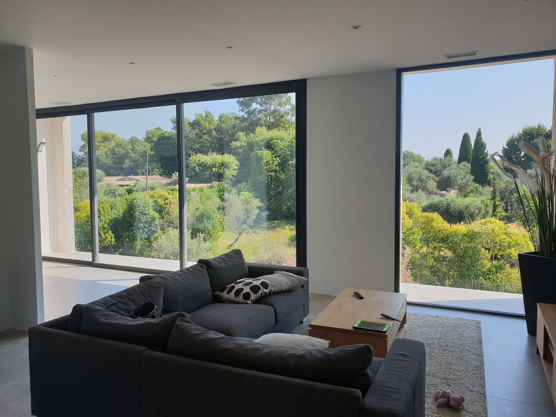 Salon avec de grandes fenêtres, canapé gris, table basse en bois.