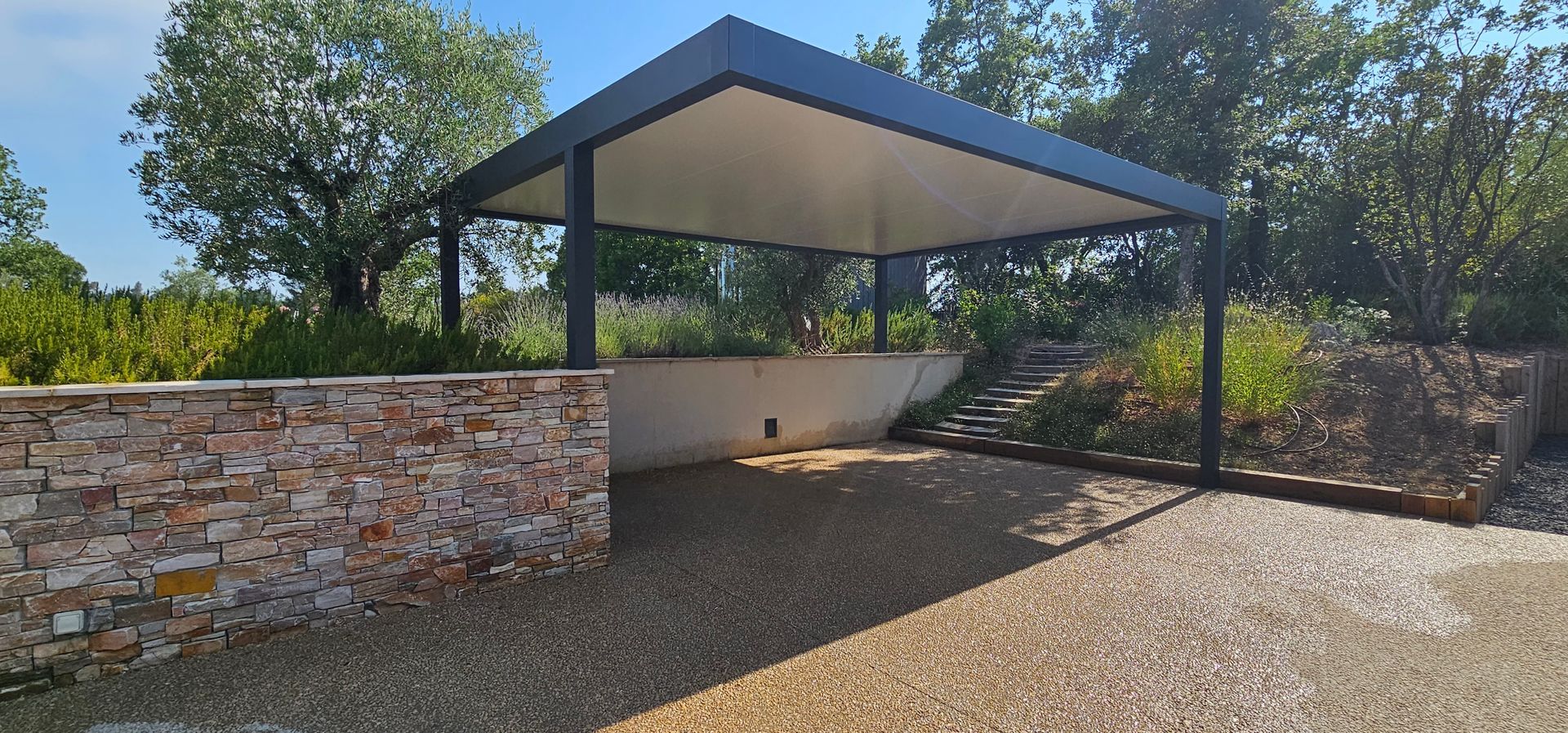 Carport pour voiture avec muret en pierre et allée gravillonnée.