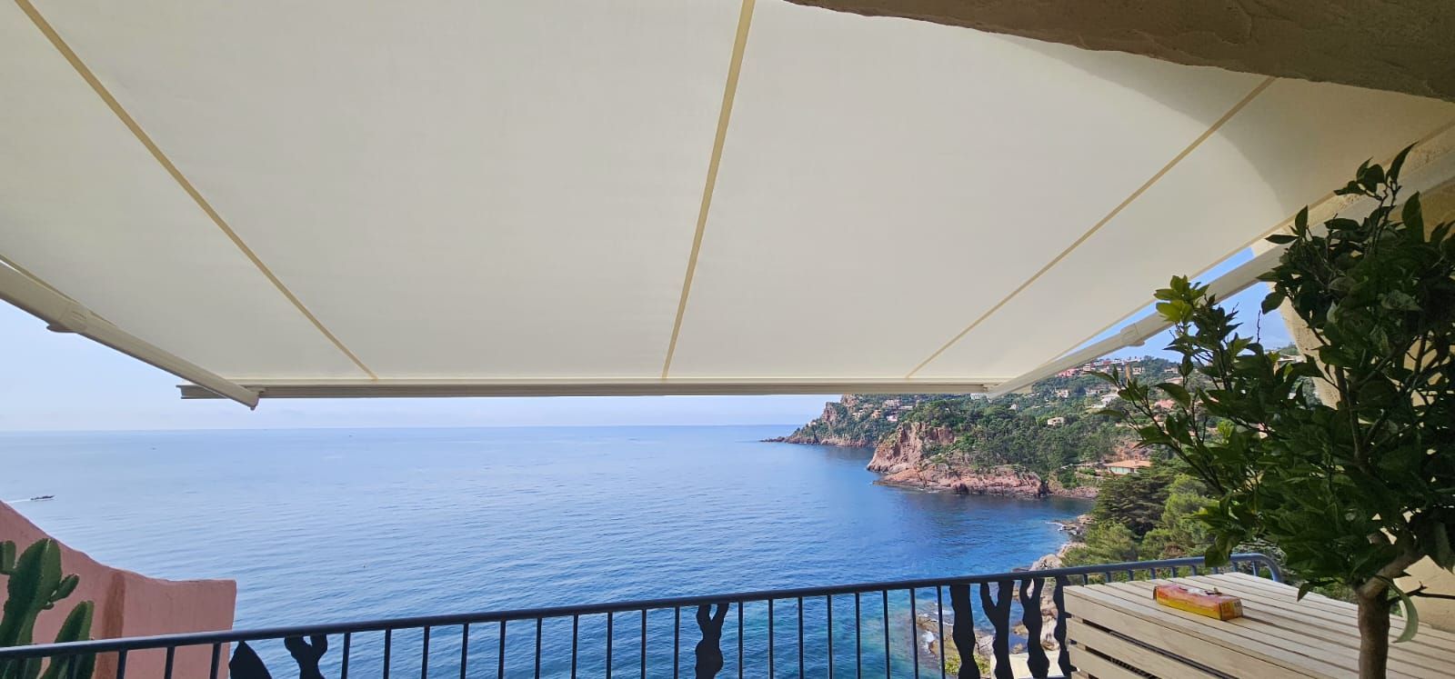 Un store rétractable protège un balcon donnant sur un océan et un littoral escarpé.