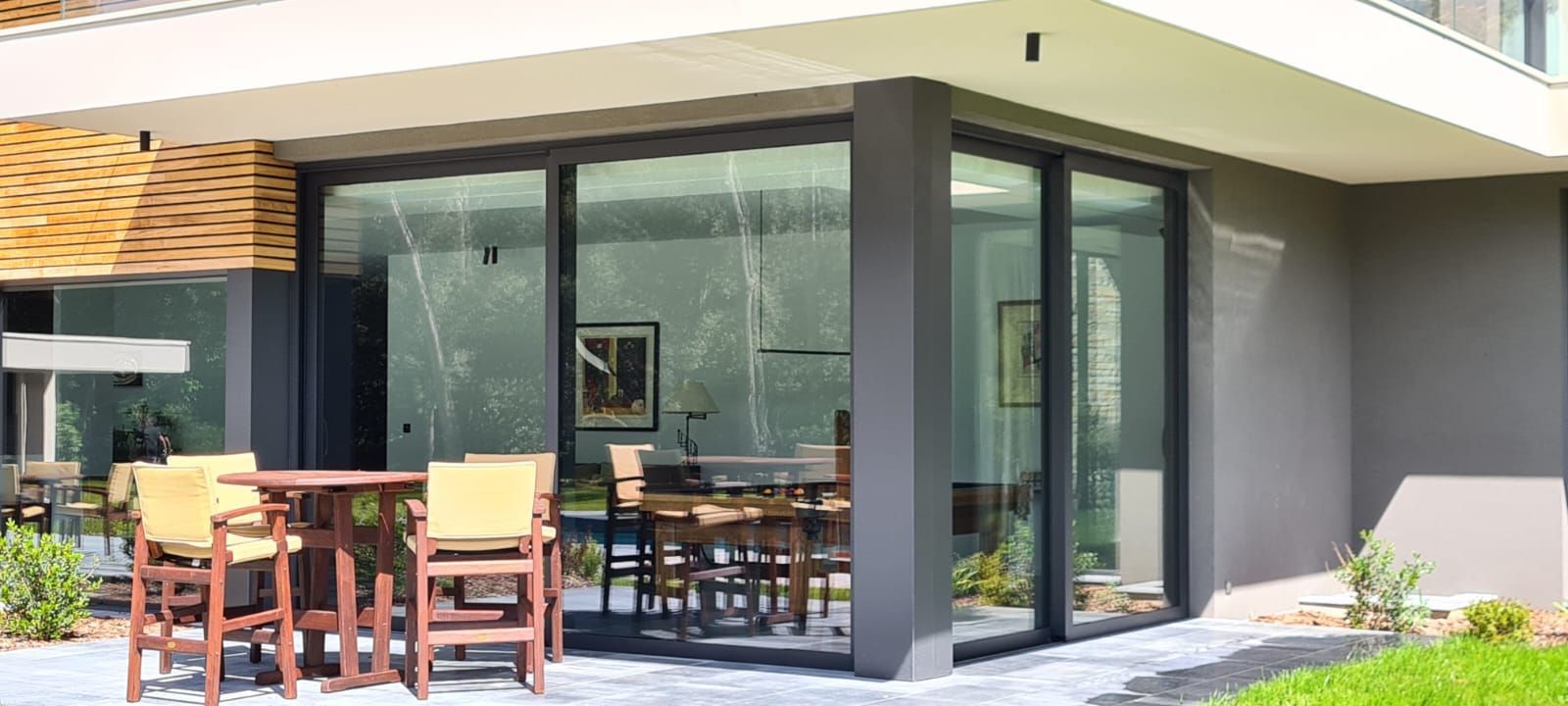 Espace repas extérieur avec une paroi vitrée, une table et des chaises en bois sur une terrasse.