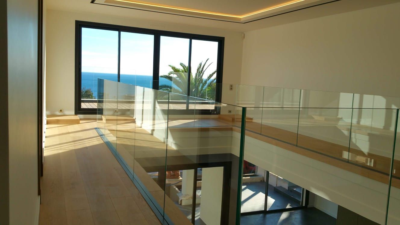 Intérieur d'une maison avec balustrades en verre offrant une vue sur l'océan depuis le deuxième étage.