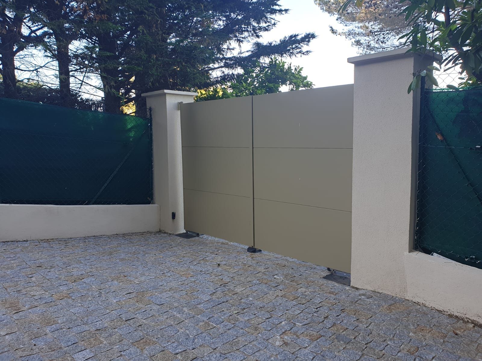 Portail d'allée beige avec piliers en pierre et sol en gravier.