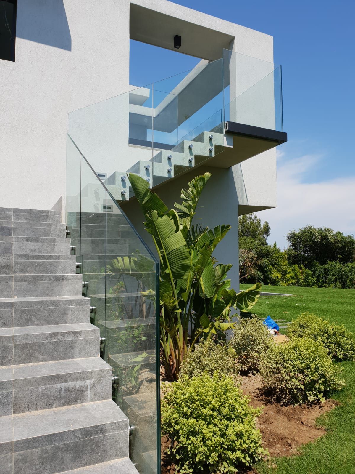 Un escalier extérieur avec rambarde en verre mène à un bâtiment blanc.
