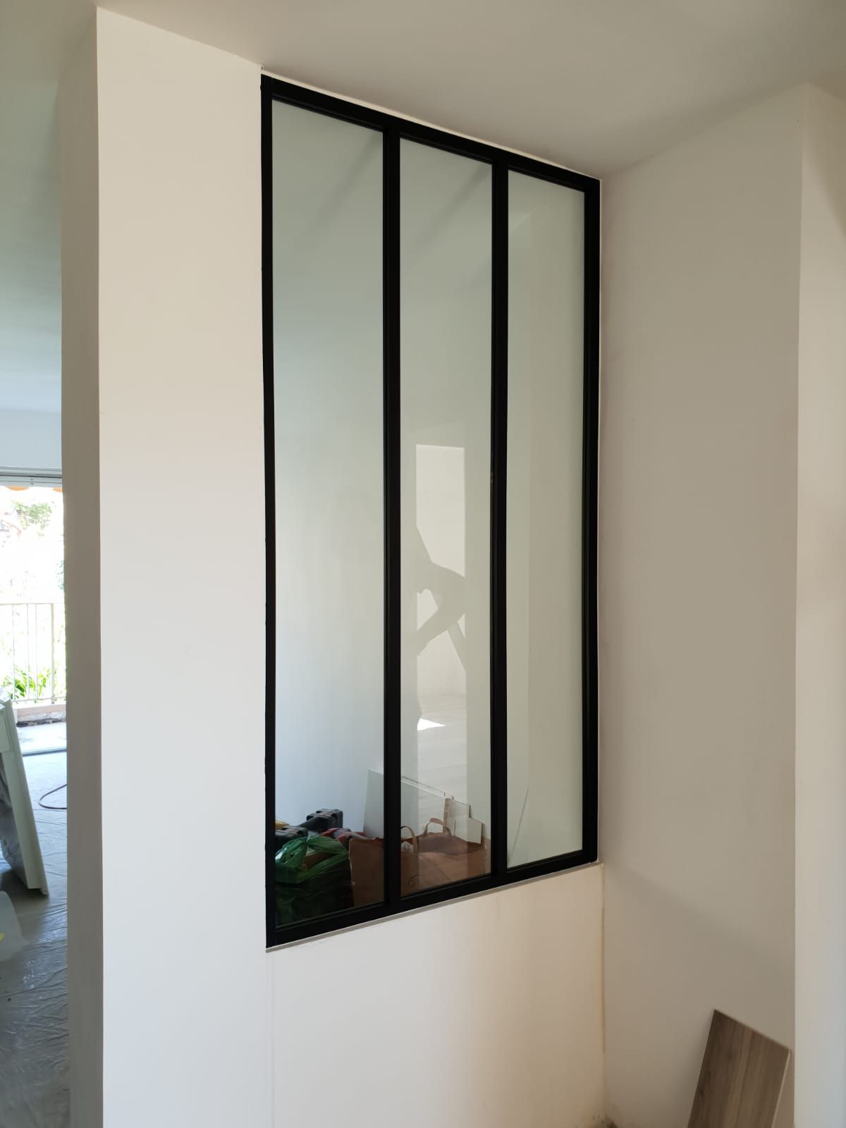 Une paroi vitrée à cadre noir sépare deux espaces aux murs blancs.