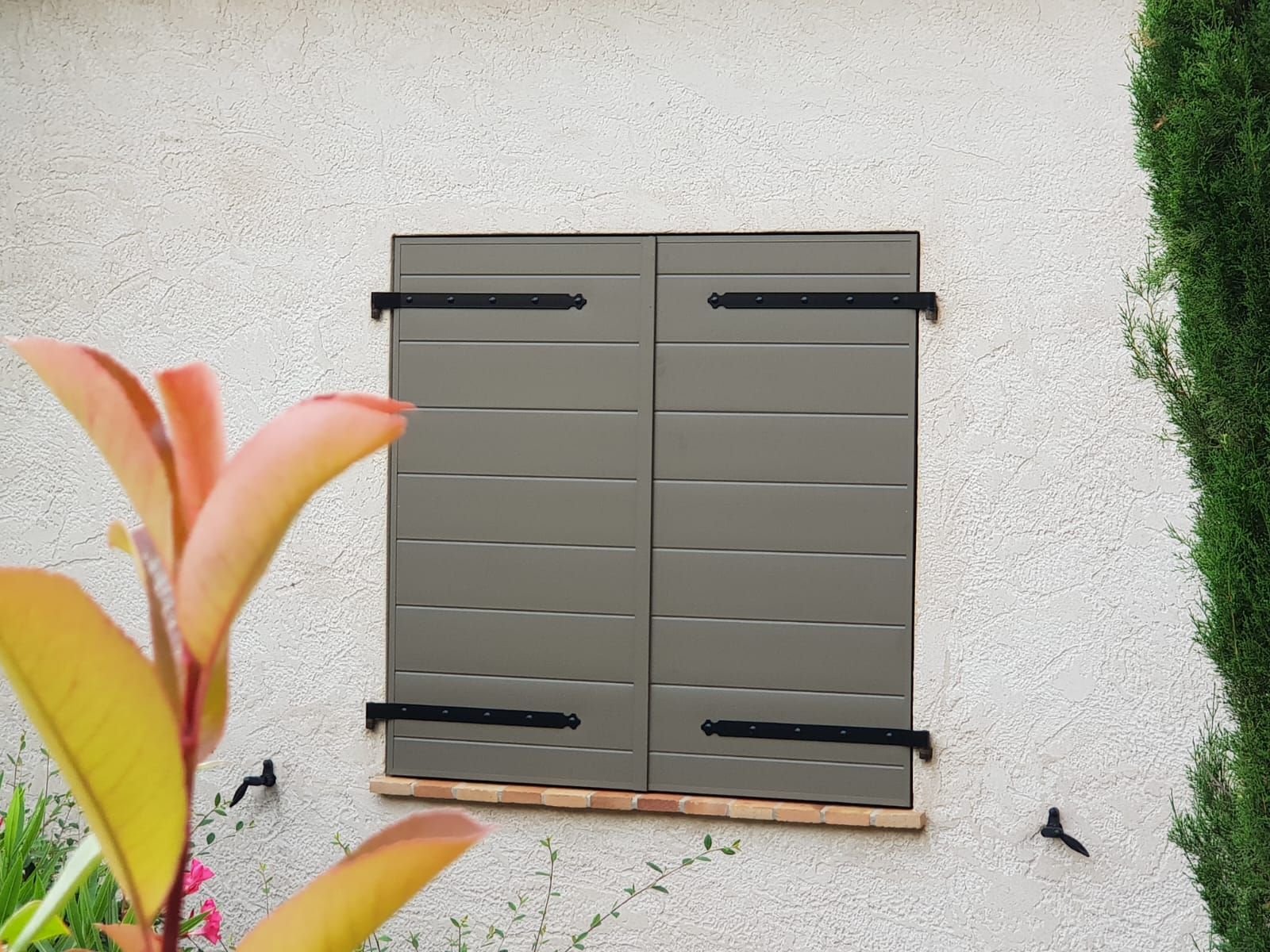Volets intérieurs gris fermés sur un mur en stuc, avec des charnières noires.