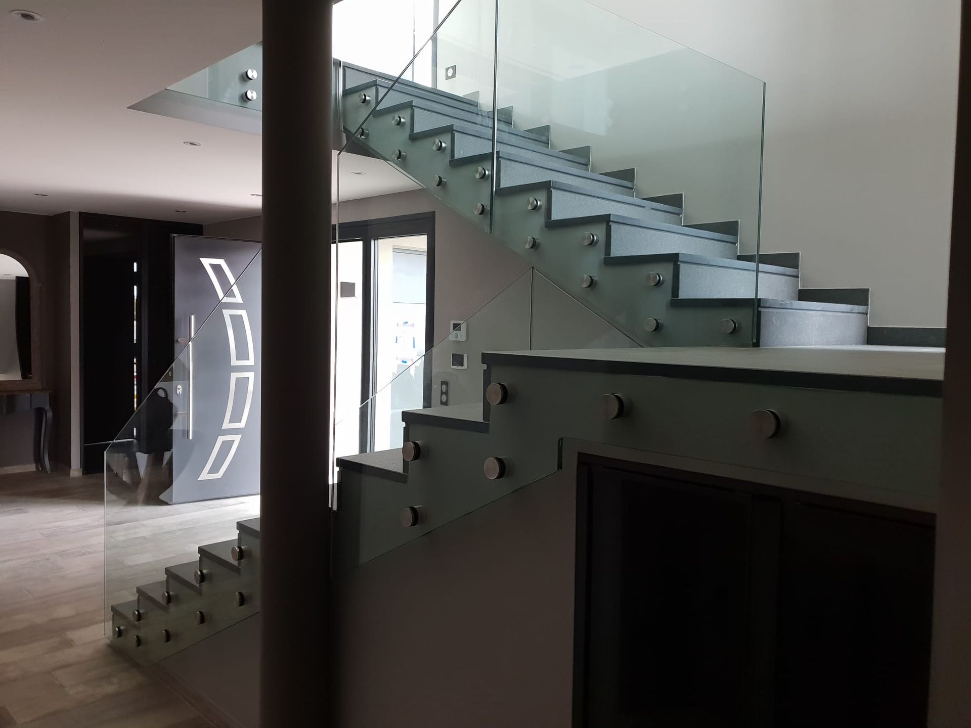 Escalier avec panneaux de verre et marches grises.
