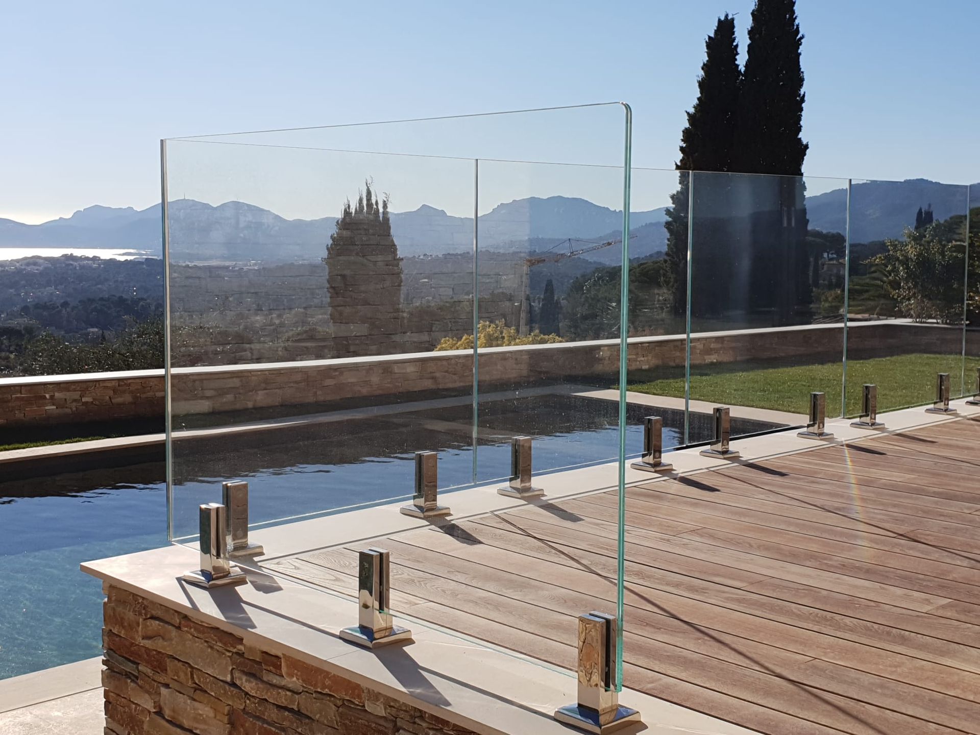 Rambarde en verre entourant une piscine sur une terrasse, avec une vue panoramique sur les montagnes.